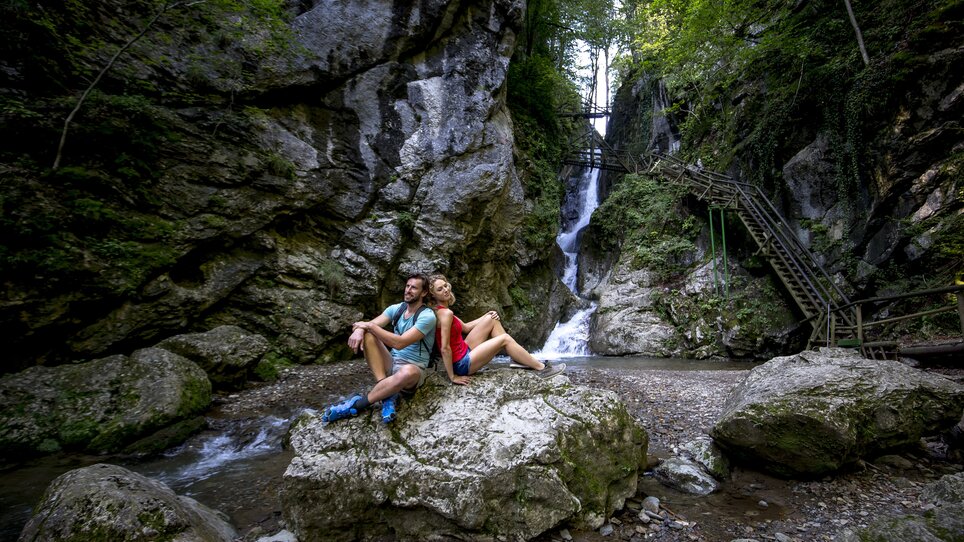 Ein Paar sitzt auf einem Felsen neben einem Wasserfall in der Kesselfallklamm. | © Region Graz - Tom Lamm