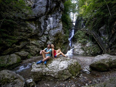 A couple sitting on a rock next to a waterfall in Kesselfallklamm. | © Region Graz - Tom Lamm