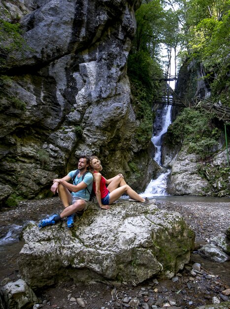 Ein Paar sitzt auf einem Felsen neben einem Wasserfall in der Kesselfallklamm. | © Region Graz - Tom Lamm