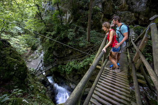Ein Paar steht auf einer Holzbrücke und schaut auf den Fluss in der Kesselfallklamm. | © Region Graz - Tom Lamm