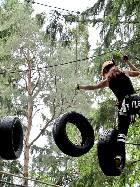 A girl balances on tires in a tree climbing course. | © Kletterpark Schöckl - Oberlaender