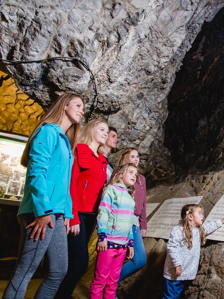 Famiglia esplora la Lurgrotte Peggau con vista sulla statua e cartelli informativi. | © TV Region Graz - Mias Photoart