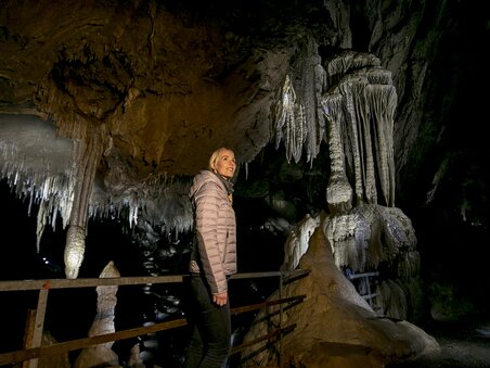 Woman stands in the Lurgrotte Semriach, amazed expression, impressive stalactites. | © Region Graz - Tom Lamm