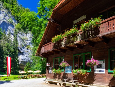 Ein Holzhaus mit Blumen über dem Eingang, umgeben von Bäumen und Felsen. | © TV Region Graz - Harry Schiffer