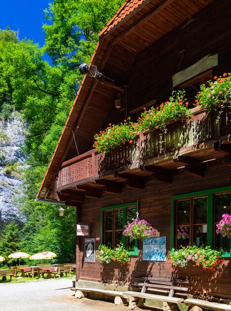 A wooden house with flowers above the entrance, surrounded by trees and rocks. | © TV Region Graz - Harry Schiffer