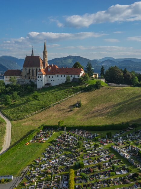 Luftaufnahme der Wallfahrtskirche Maria Strassengel mit einem Friedhof im Vordergrund. | © TV Region Graz - PicFly