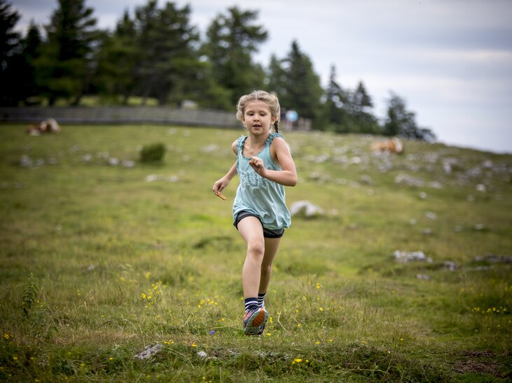 Ein Mädchen läuft fröhlich über eine grüne Wiese auf dem Schöckl. | © Region Graz - Tom Lamm