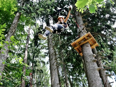 Una persona dondola tra gli alberi in un parco avventura.