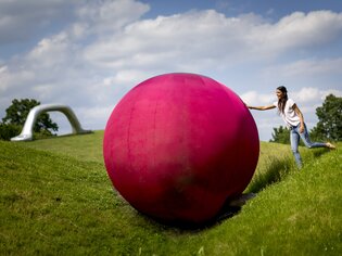 Eine Frau mit einer großen pinken Kugel im Österreichischen Skulpturenpark. | © Region Graz - Tom Lamm