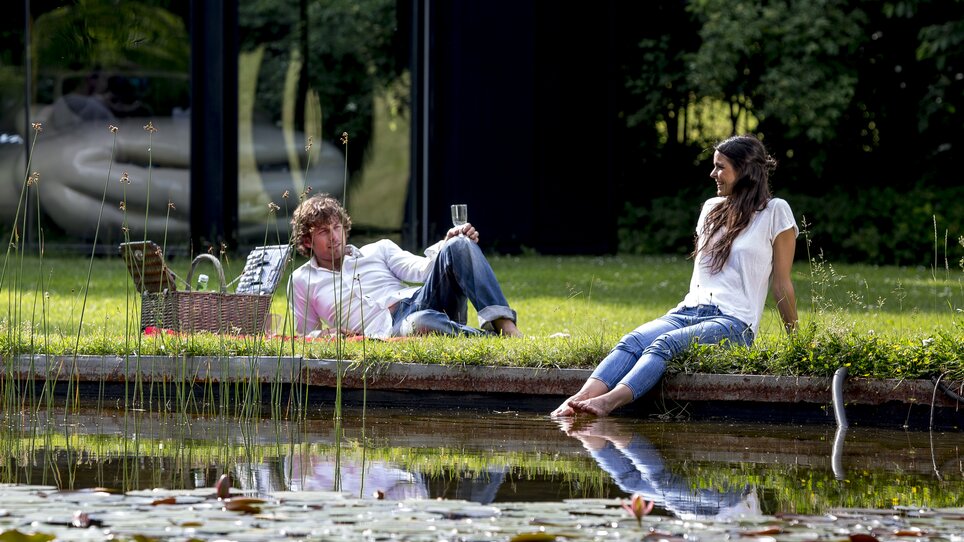 Zwei Personen entspannen am Ufer eines Gewässers im österreichischen Skulpturenpark. | © Region Graz - Tom Lamm