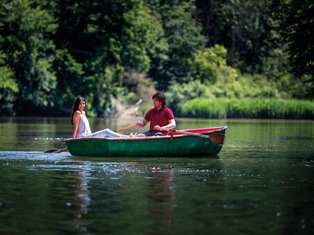 Ein Paar rudert in einem grünen Boot auf stillem Wasser umgeben von Bäumen. | © Region Graz - Tom Lamm
