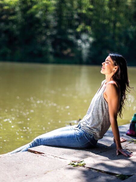 Eine Frau sitzt entspannt am Ufer eines ruhigen Gewässers. | © Region Graz - Tom Lamm