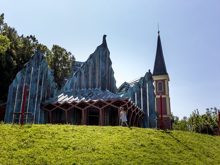 Außensicht der Jakobuskirche mit spitzem Turm und bunten Elementen. | © Region Graz - Tom Lamm