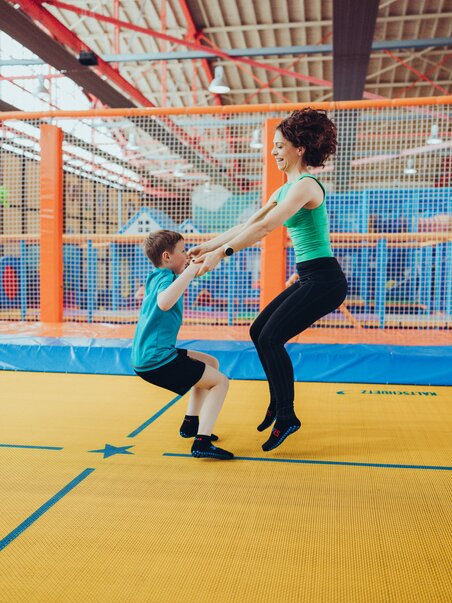 Eine Frau hilft einem Kind beim Springen auf einem Trampolin. | © Lex Karelly