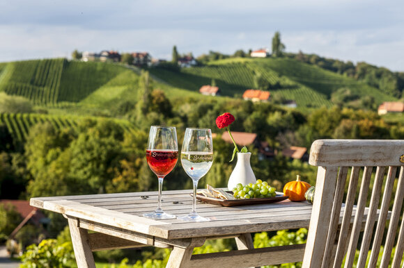 Due bicchieri di vino su un tavolo con vista sui vigneti. | © Steiermark Tourismus - ikarus
