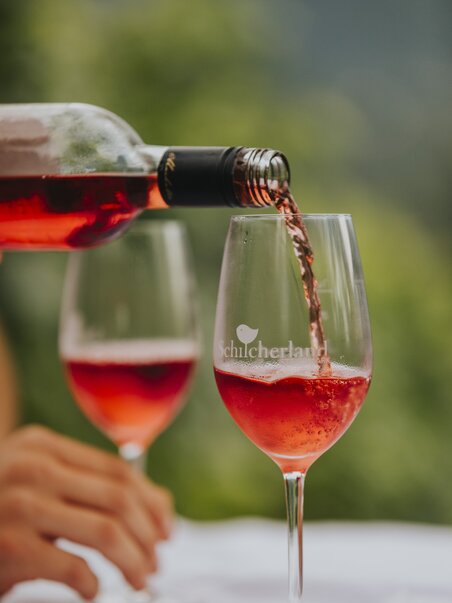 Due calici di vino vengono riempiti con Schilcher rosato da una bottiglia – specialità regionale della Stiria occidentale in Austria. | © Schilcherland Steiermark - Lupi Spuma