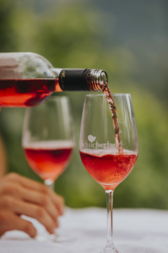 Zwei Weingläser werden mit roséfarbenem Schilcherwein aus einer Flasche gefüllt – regionaler Wein aus der Weststeiermark. | © Schilcherland Steiermark - Lupi Spuma