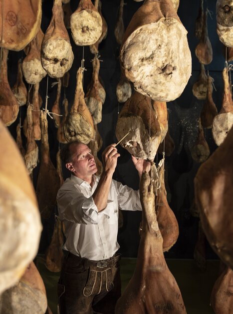 Ein Mann prüft Schinken in einer Reifekammer. | © Vulcano