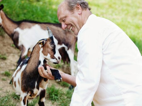 Ein lächelnder Mann interagiert fröhlich mit einer Ziege. | © Zotter Schokolade