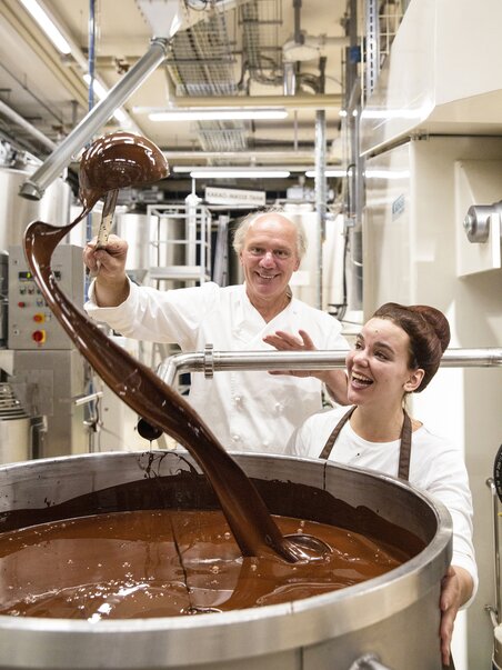 Zwei Personen arbeiten in einer Schokoladenfabrik mit flüssiger Schokolade. | © Zotter Schokolade