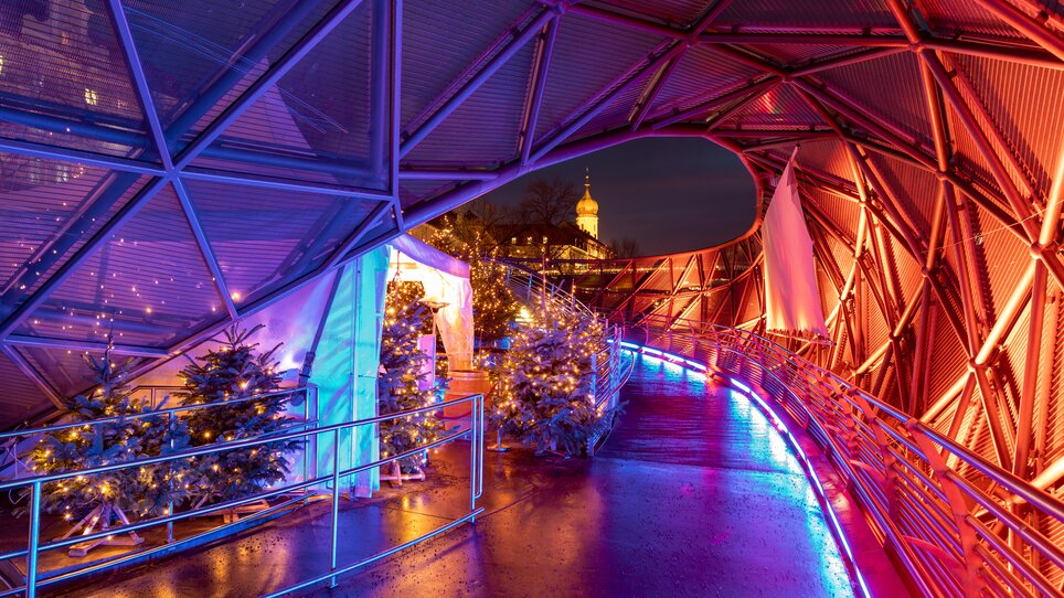 Futuristic path with colorful lights and Christmas trees on the Island in the Mur in Graz. | © Graz Tourismus - Harry Schiffer I Lichtkonzept: Ochoresotto  
