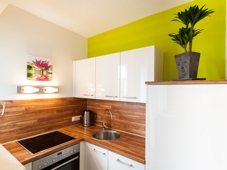 Cucina compatta con superfici in legno, armadi bianchi e accento verde. | © R. Kaiser