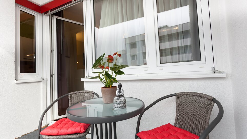A balcony with round chairs, table, and potted plants. | © R. Kaiser
