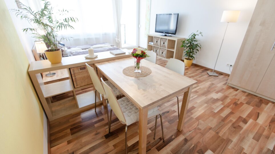 A modern living room featuring a dining table, plants, and a TV. | © R. Kaiser