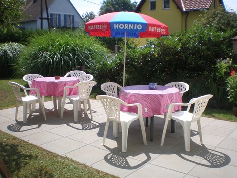 Cozy garden area with tables and chairs under an umbrella. | © Appartement Anne-Marie