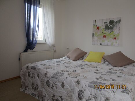 Bedroom with a double bed and flower painting on the wall. | © Appartement Anne-Marie