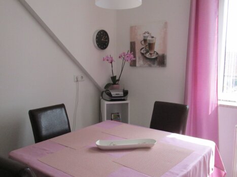 Dining area with table, chairs, a clock, and an orchid. | © Appartement Anne-Marie