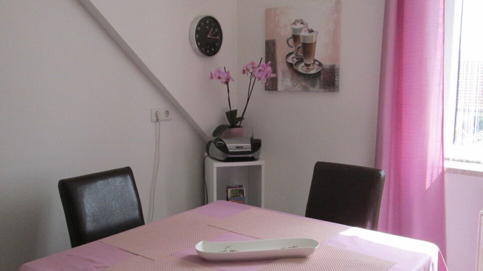 Zona pranzo con tavolo, sedie, un orologio e un'orchidea. | © Appartement Anne-Marie