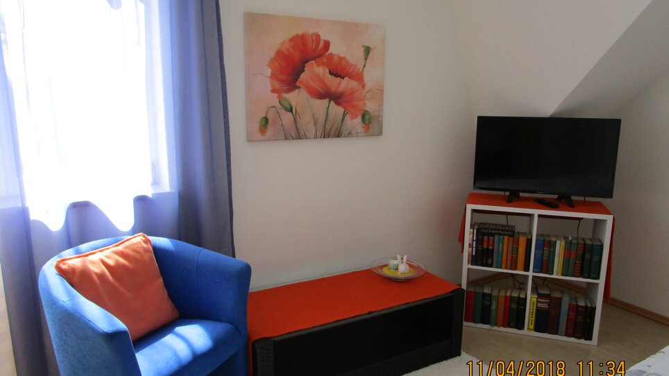 Angolo accogliente con poltrona blu, TV e libreria. | © Appartement Anne-Marie