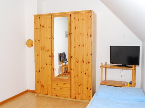A simple room with a wooden wardrobe, TV, and a bed. | © Appartement Rupp