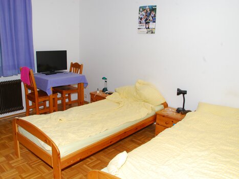 A simple room with two beds, a table, and a TV. | © Appartement Rupp