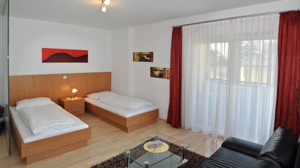 Camera luminosa con due letti singoli e un divano. | © Steinbichler