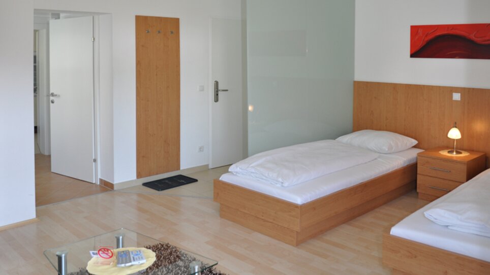 Alloggio luminoso con due letti, tavolo in vetro e arredamento moderno. | © Steinbichler