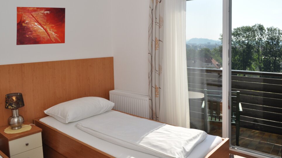 Una stanza luminosa con un letto singolo, balcone e vista sul verde. | © Steinbichler