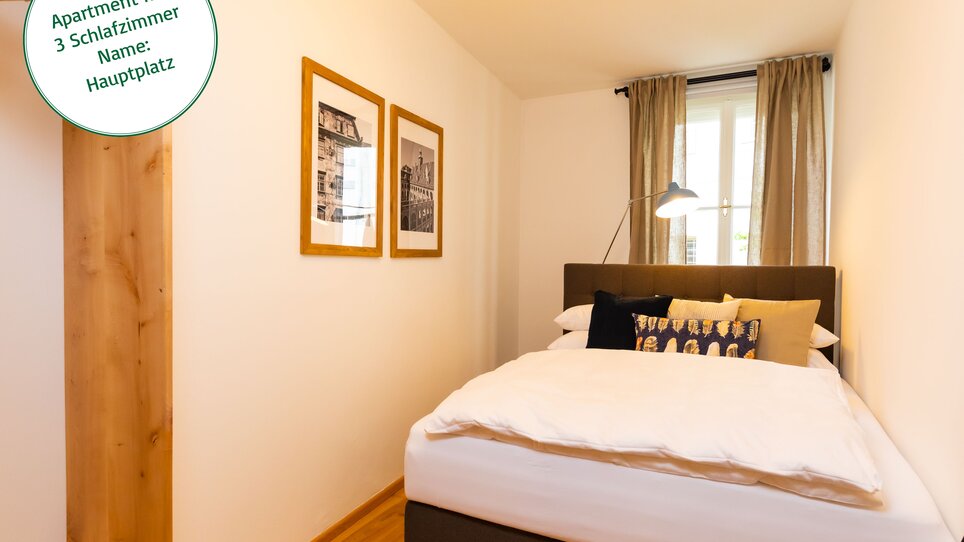 Camera da letto con un letto matrimoniale, immagini sulla parete e tende di colore beige