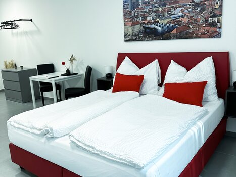 A bedroom with red accents and a picture with a view of Graz. | © Grazora Living