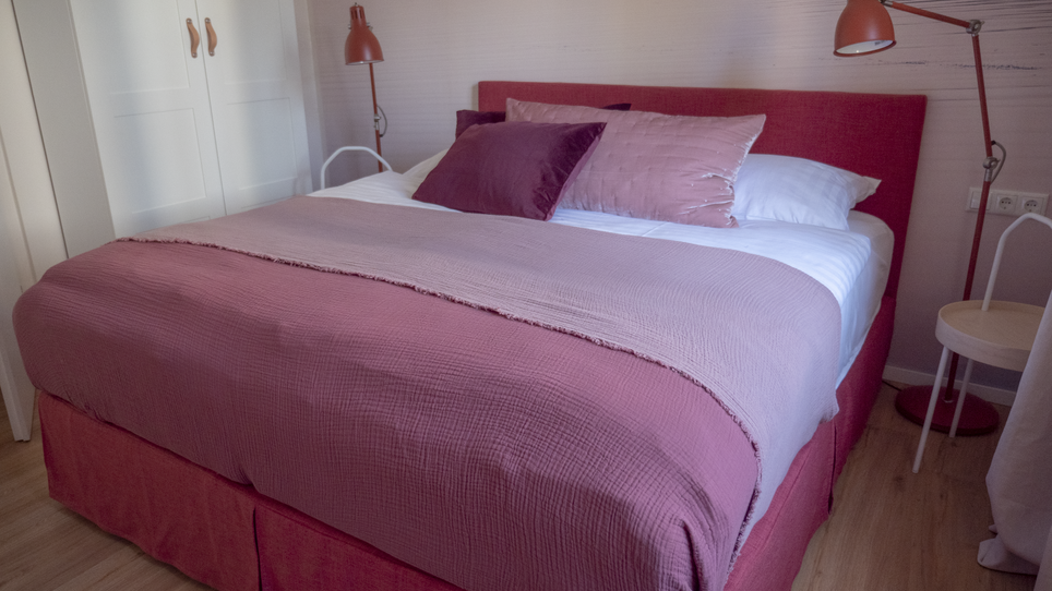 Un letto con cuscini viola e bianchi in una camera da letto moderna. | © GrazRentals