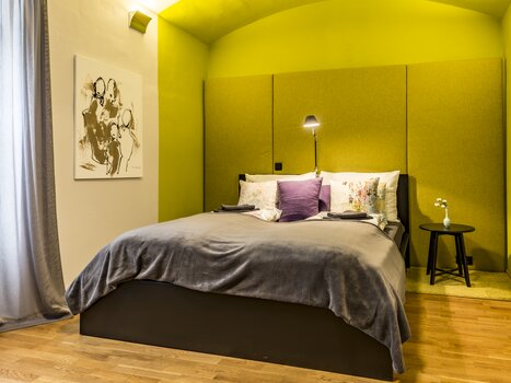 Una camera da letto con un letto, accentuazione verde della parete e opere d'arte. | © GrazRentals