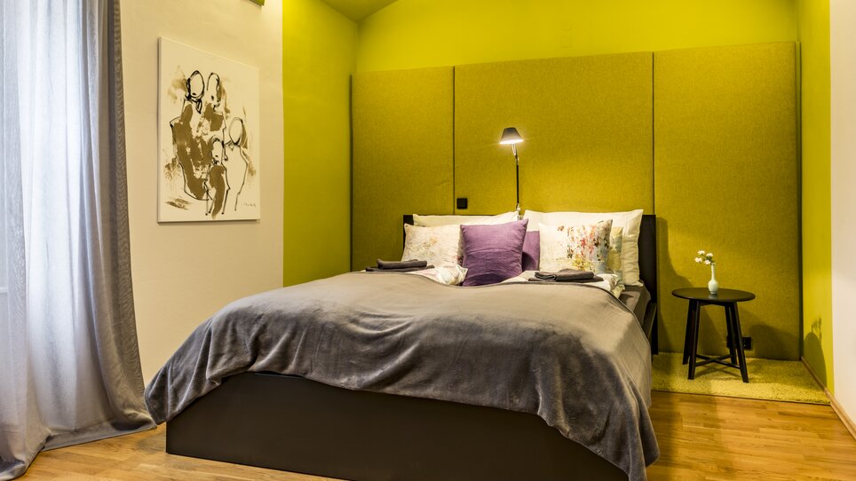 Una camera da letto con un letto, accentuazione verde della parete e opere d'arte. | © GrazRentals