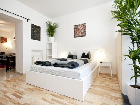 Bright bedroom with two beds, plants, and artworks on the wall. | © Grocholl