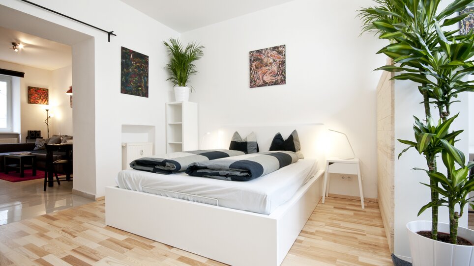 Camera da letto luminosa con due letti, piante e opere d'arte sulle pareti. | © Grocholl