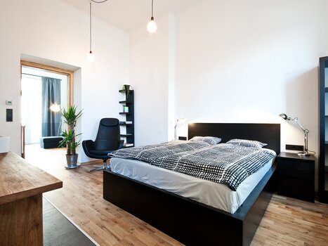 A bright bedroom with a double bed, chair, and plants. | © Grocholl