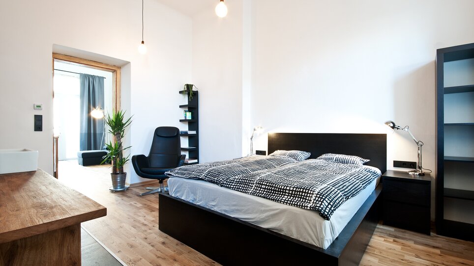 Una camera luminosa con letto matrimoniale, sedia e piante. | © Grocholl