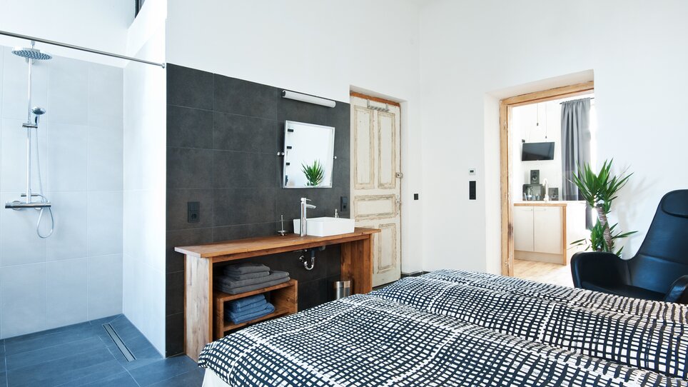 Una camera con doccia, lavandino e un letto in primo piano. | © Grocholl