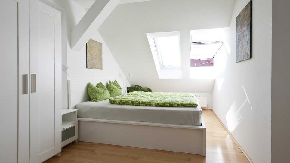 Camera luminosa con biancheria da letto verde e finestre a tetto. | © Grocholl