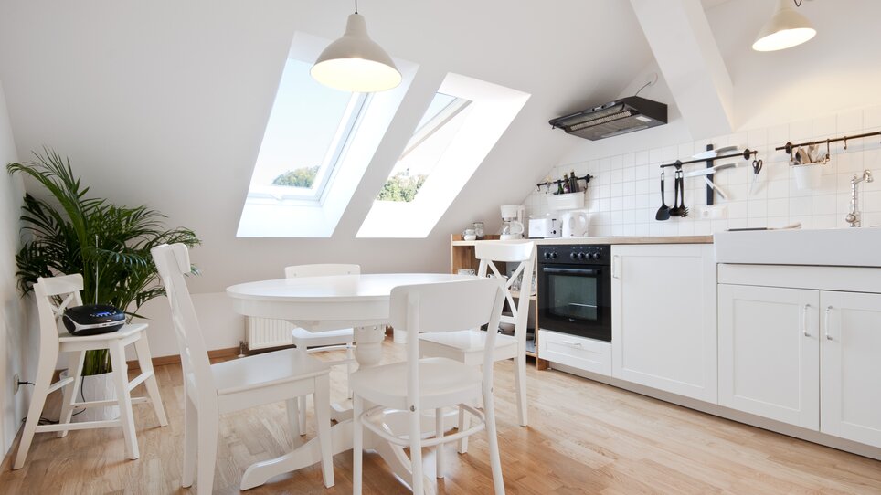 Cucina nel sottotetto con finestre e mobili bianchi. | © Grocholl